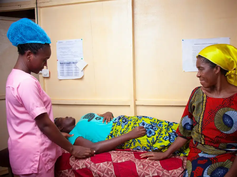 A nurse tending a patient lying down while a relative sits beside them