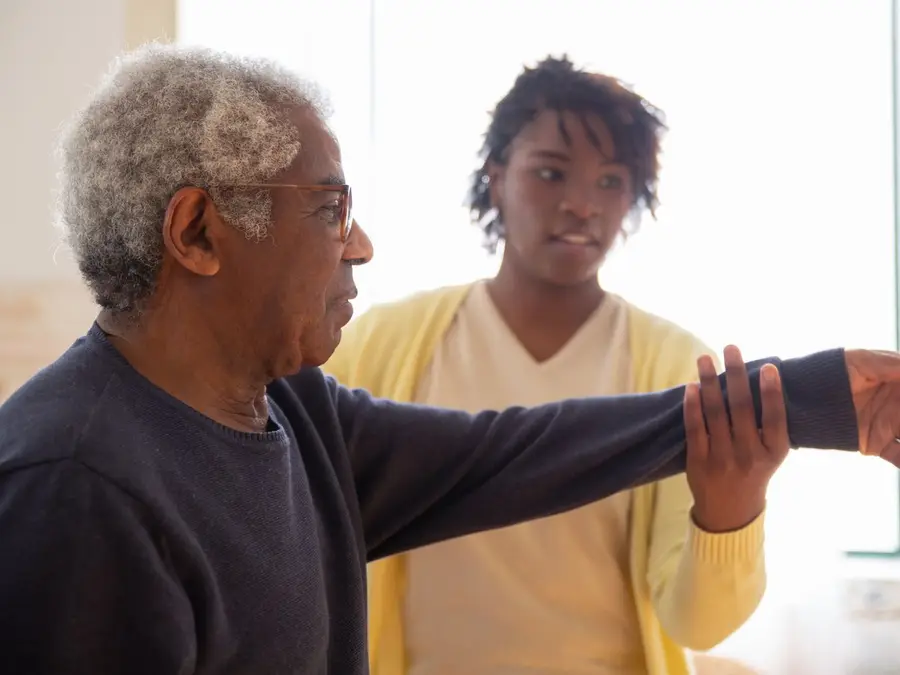A carer supporting an older man's arm as he stretches it out