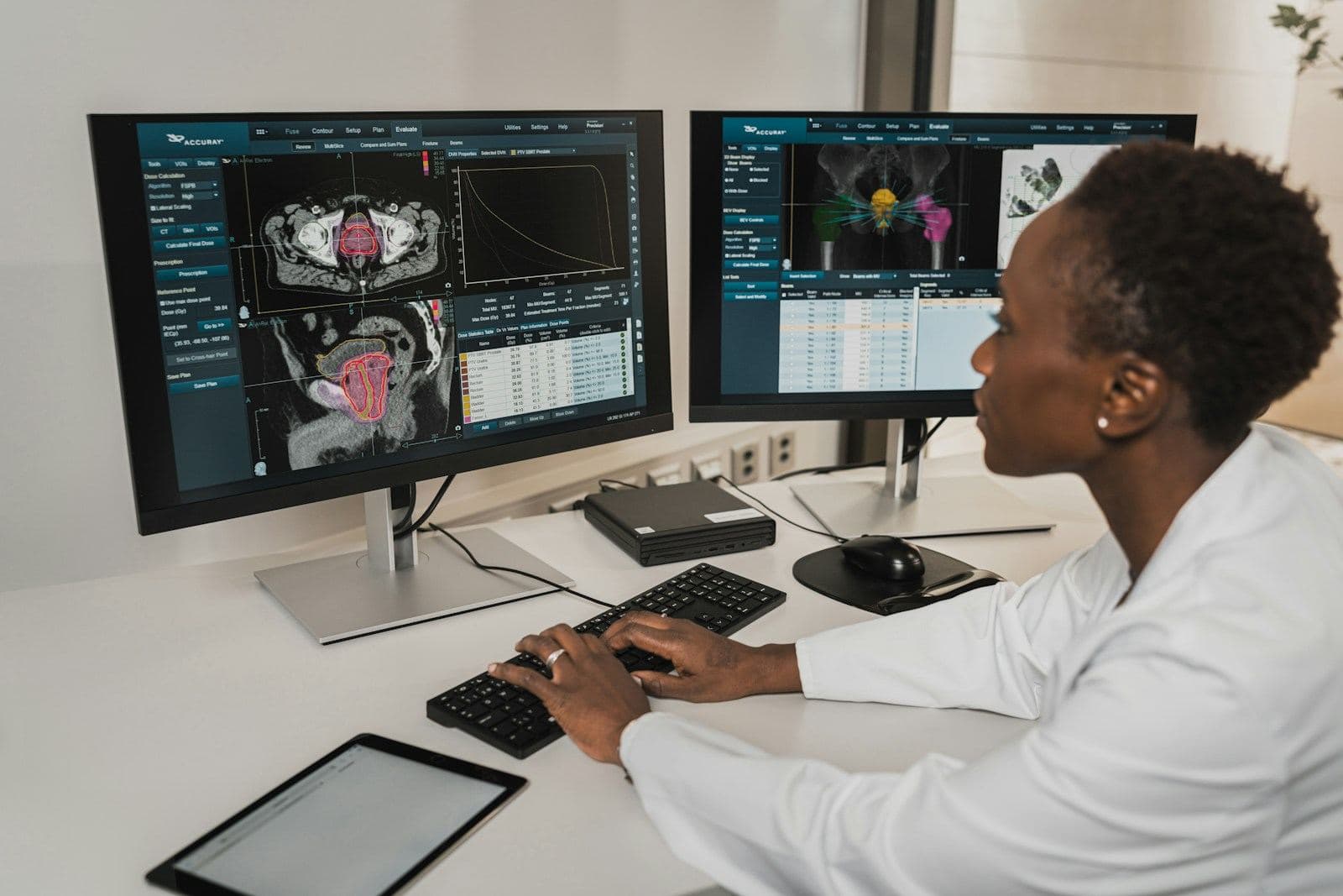 A clinician in a white coat reviewing scan images on two screens.