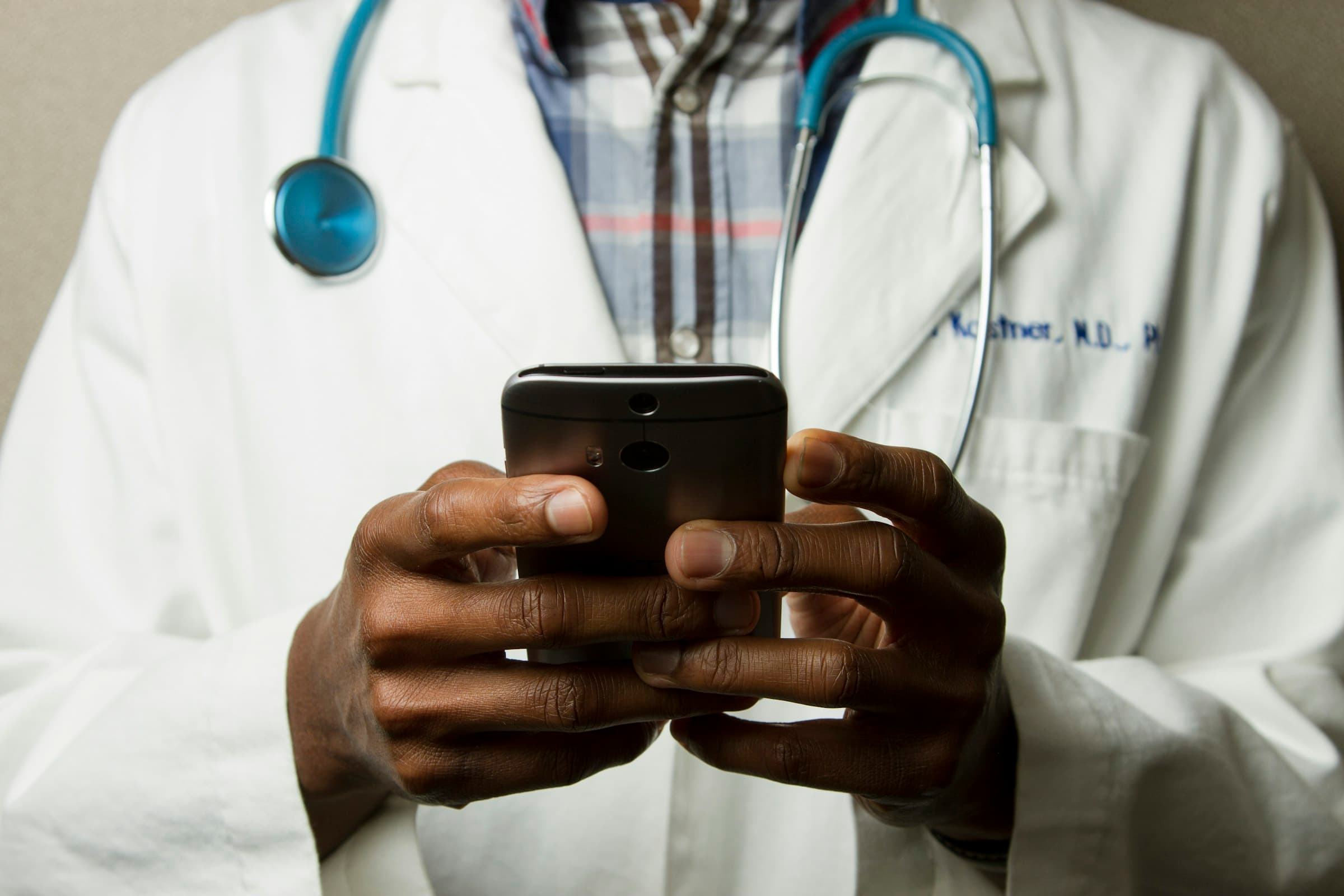 A doctor in a white coat holding a phone.