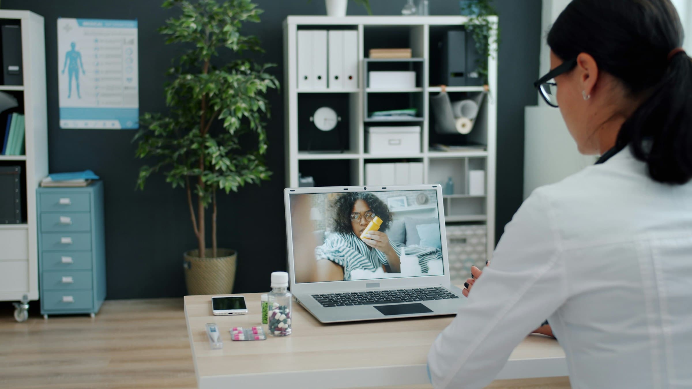 A doctor on a video call with a patient, shown on a laptop screen.