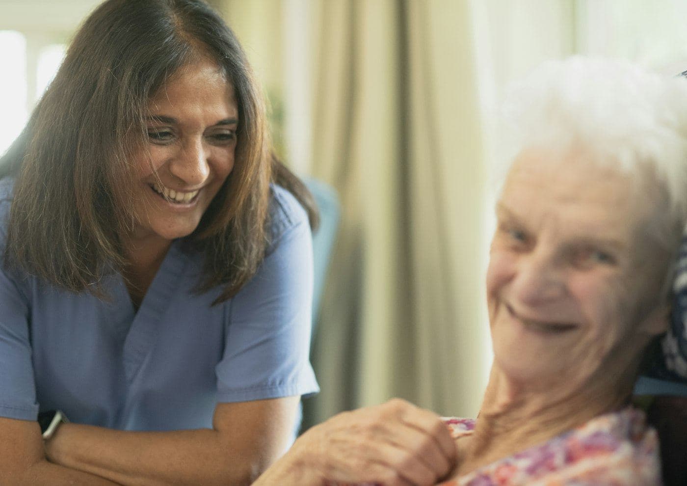 A nurse sitting beside an elderly patient, holding her hand.